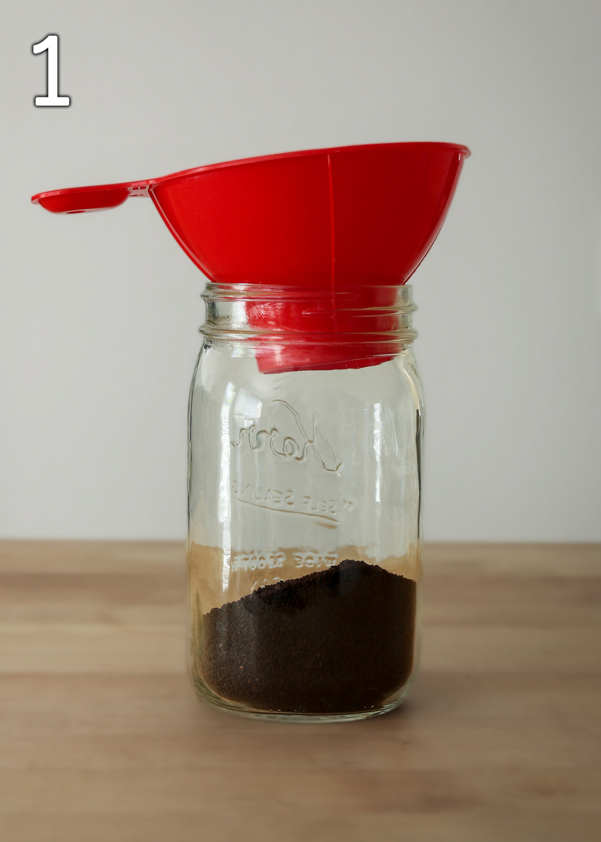 coffee grounds in glass jar with red wide mouth funnel.