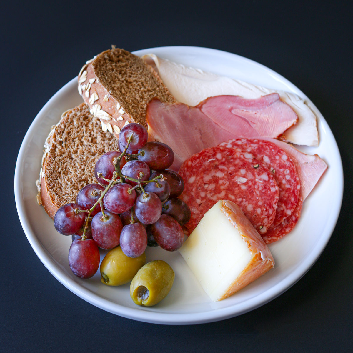 small plate with cheese, meat, fruit, bread, and olives.