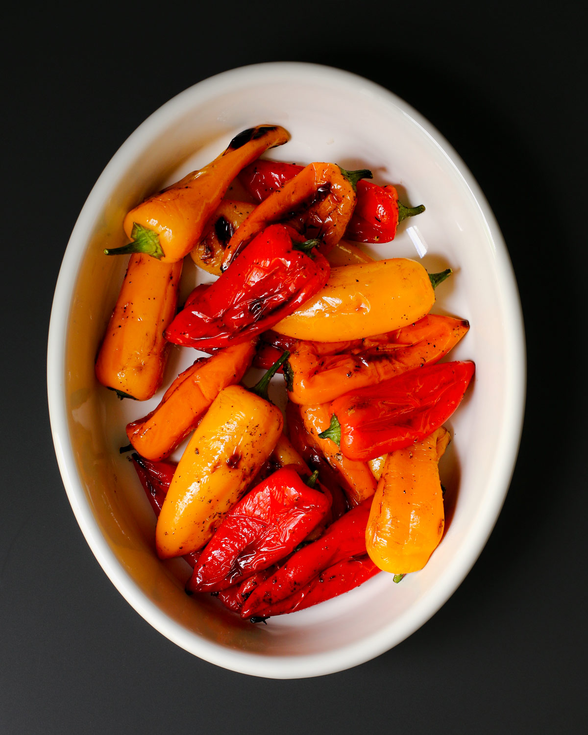grilled tri-color peppers in oval serving dish on black table.