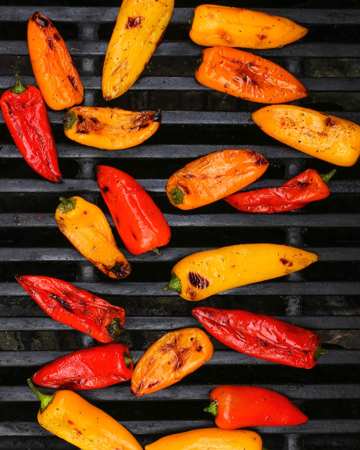 red, yellow, and orange grilled peppers on a gas grill.