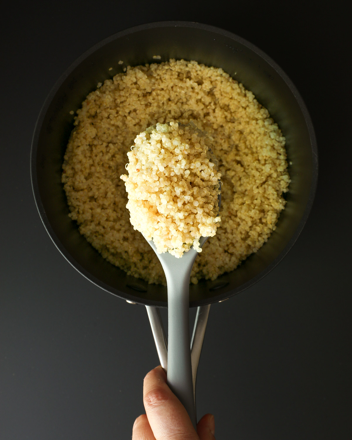 overhead shot of quinoa in pot with gray spoonful resting on handle.