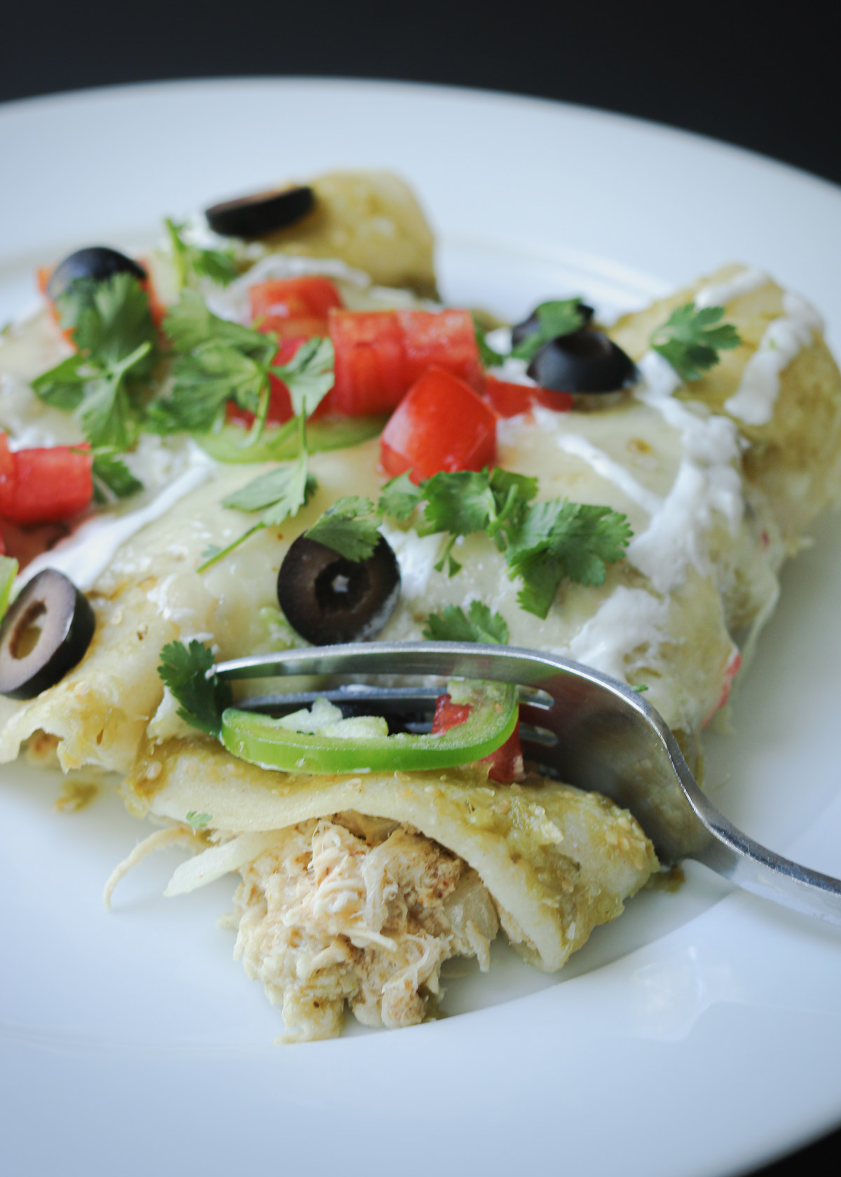 fork digging into a chicken cream cheese enchilada on a round plate.