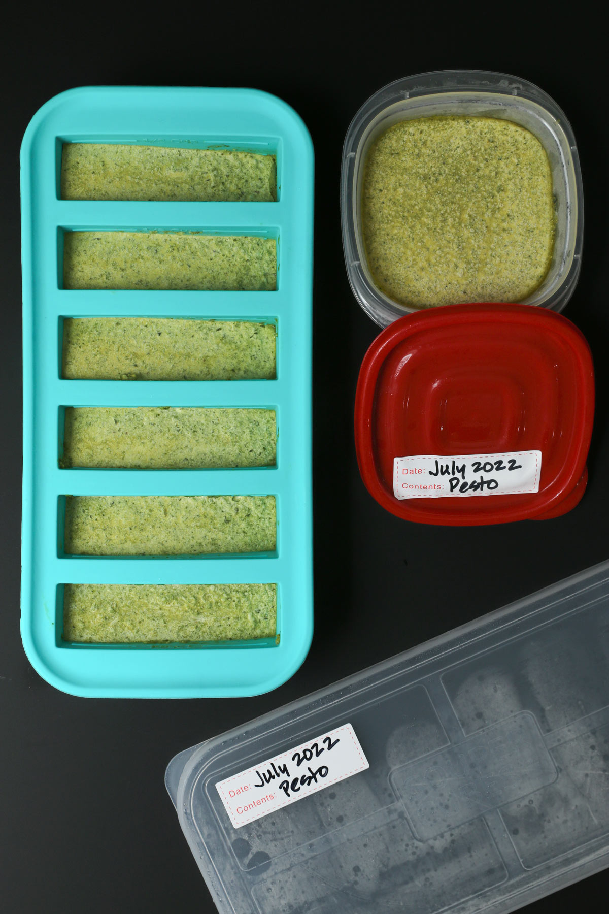 frozen pesto in souper cubes as well as small food container with a red lid.