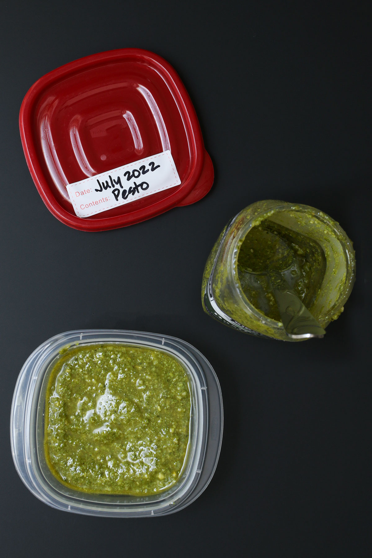 pesto tub with spoon next to a small food container with labeled red lid.