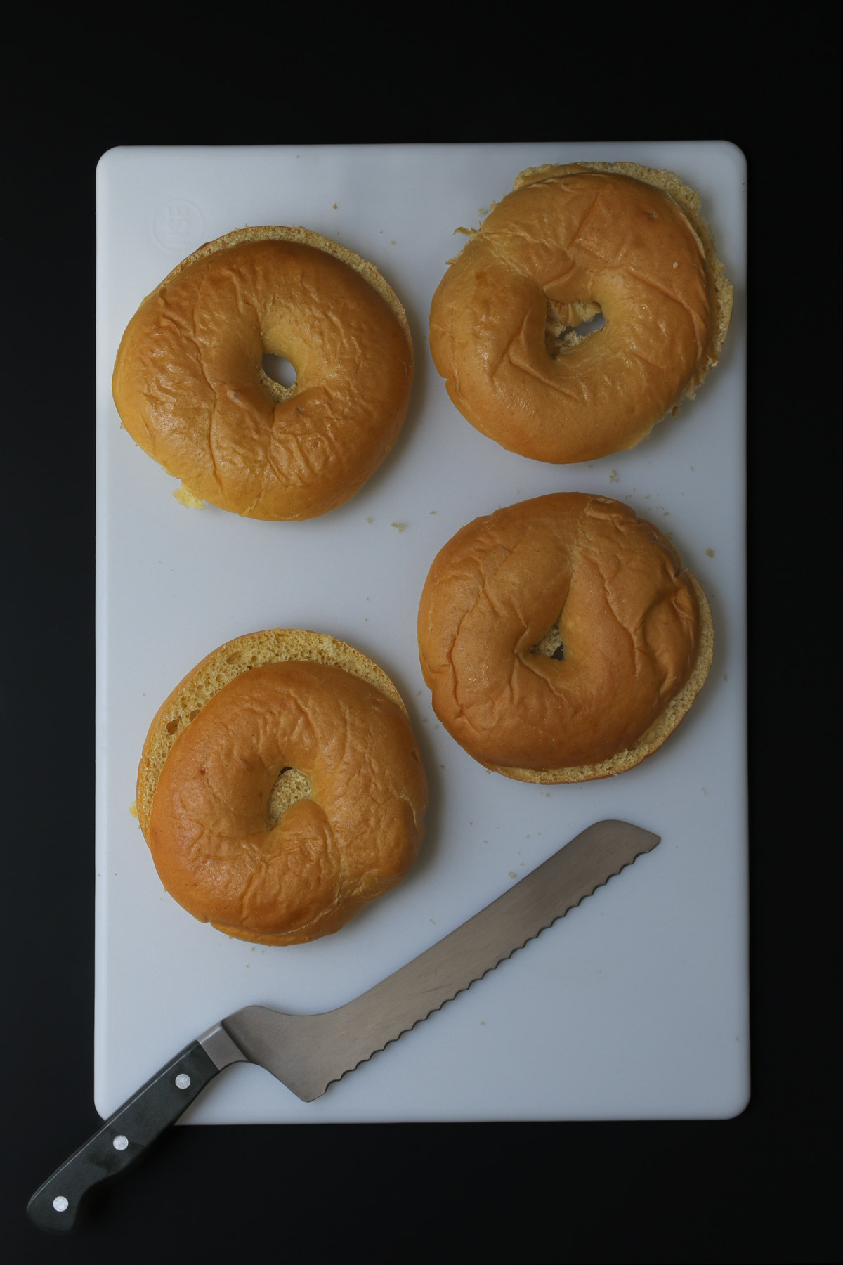 cutting bagels on cutting board with bread knife.