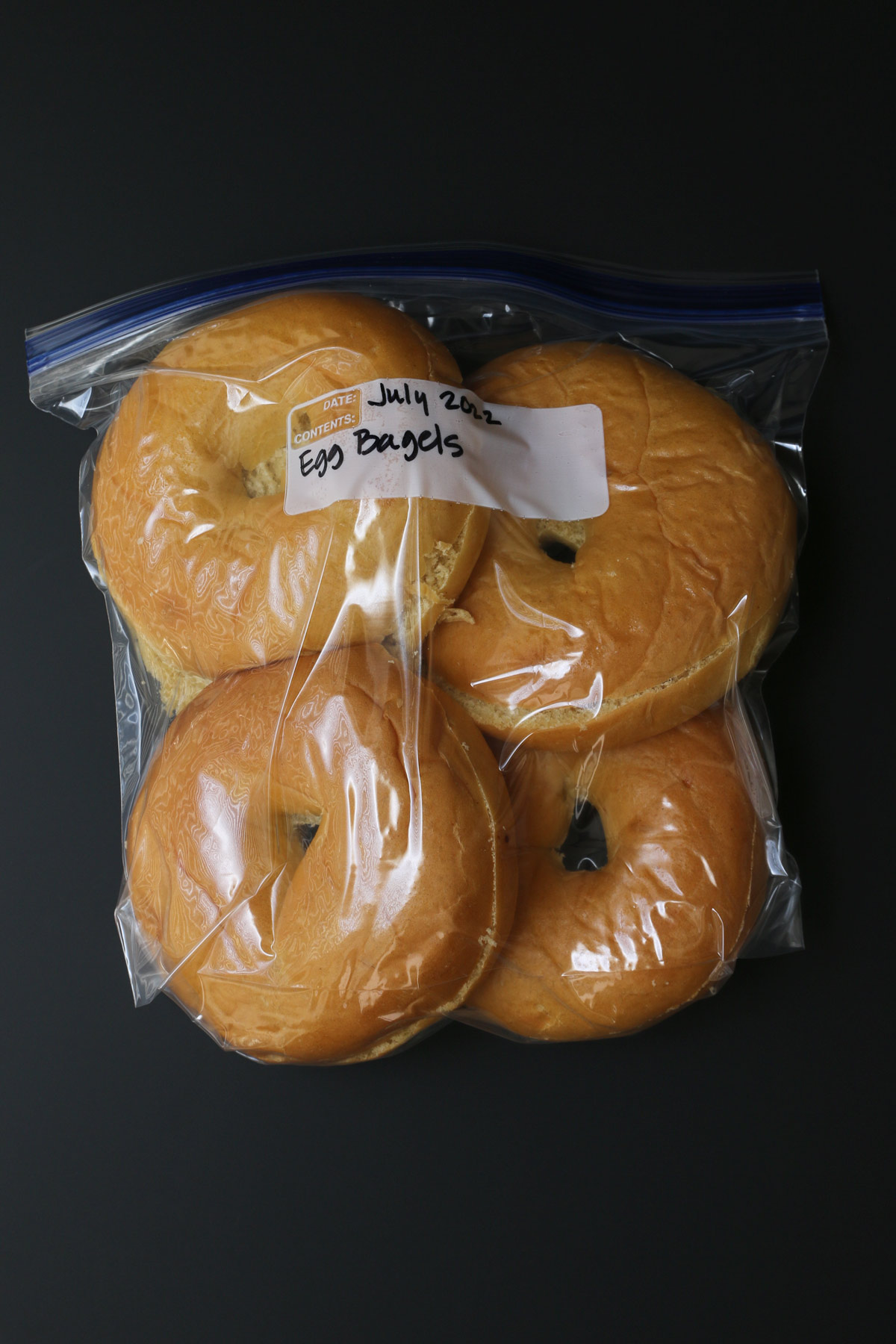 sliced bagels in labeled bag on black table.