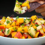 mango peach salsa on a blue corn tortilla chip over a bowl of salsa.