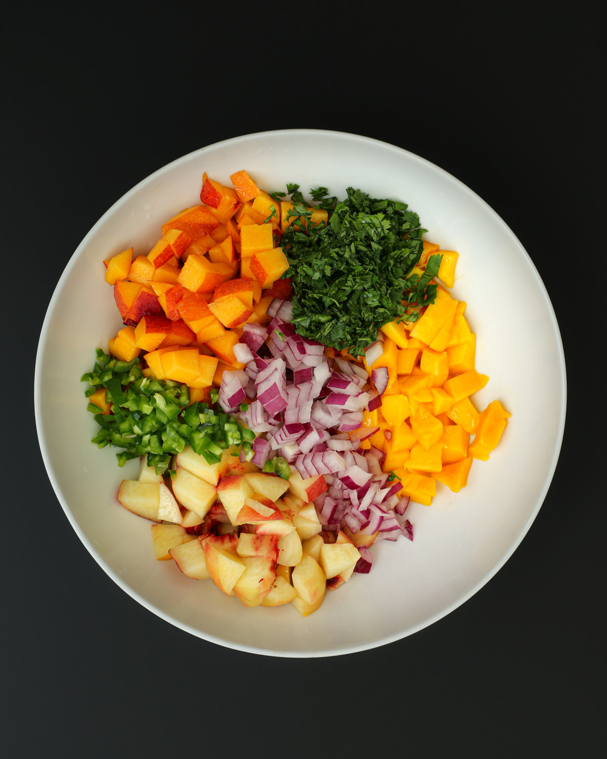 ingredients for mango peach salsa in white bowl.