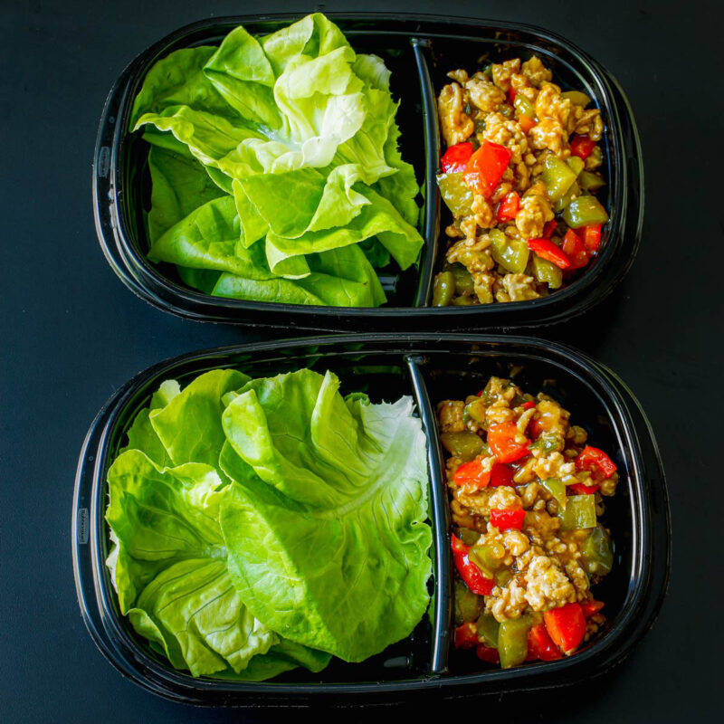 two black divided meal prep boxes with lettuce leaves on one side and turkey filling on the other.