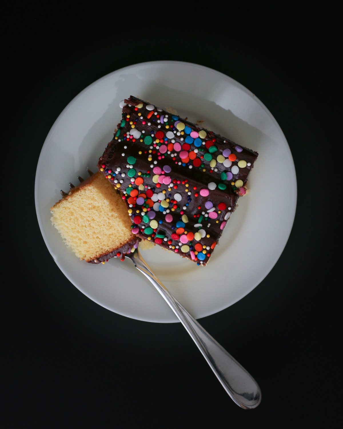 square of yellow cake on plate with chocolate frosting and sprinkles.