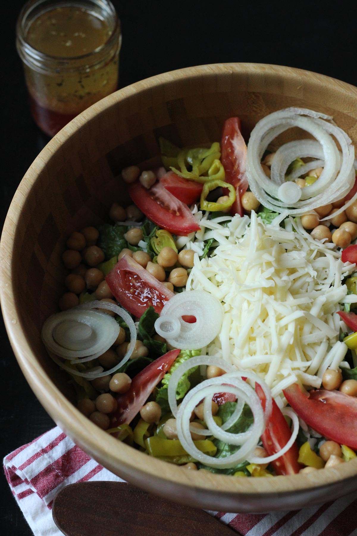 antipasto salad in wooden bowl with dressing cup nearby.