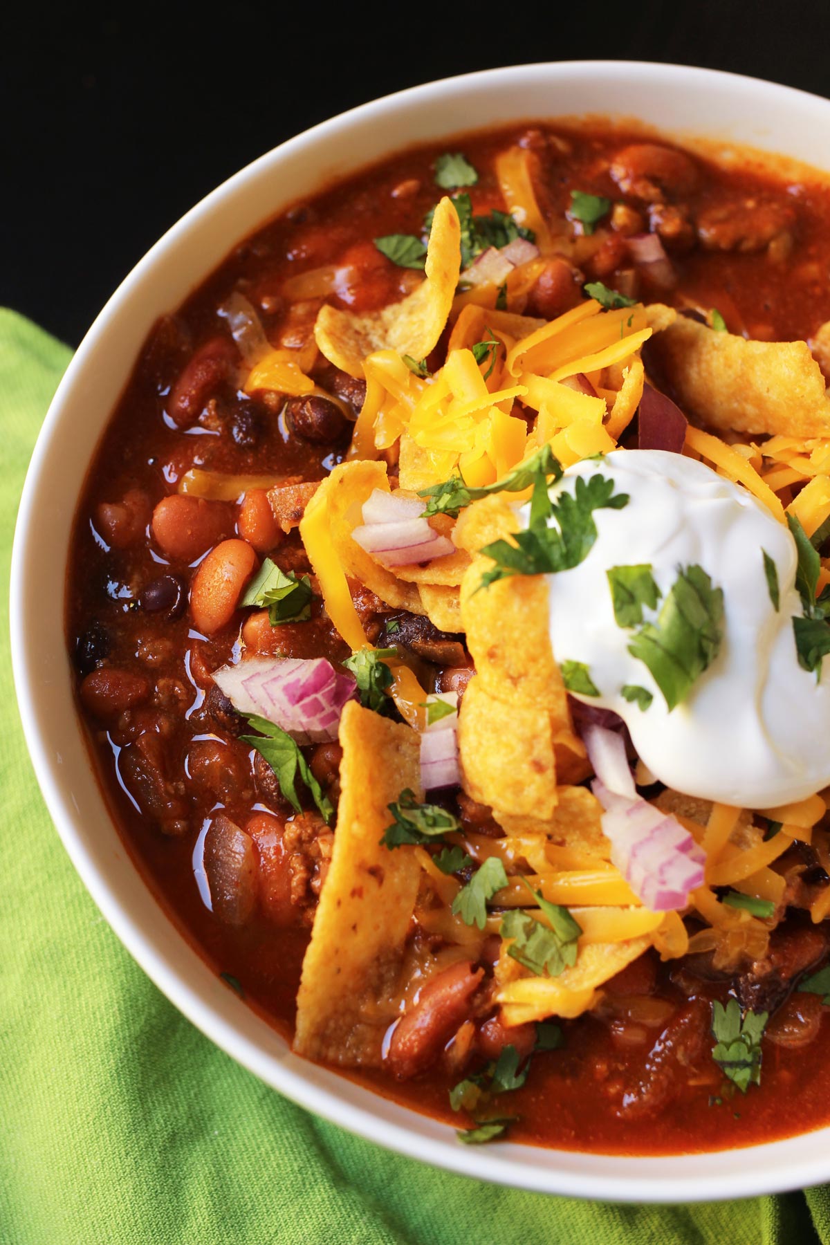 bowl of chili topped with fritos, sour cream, red onion, and chopped cilantro.