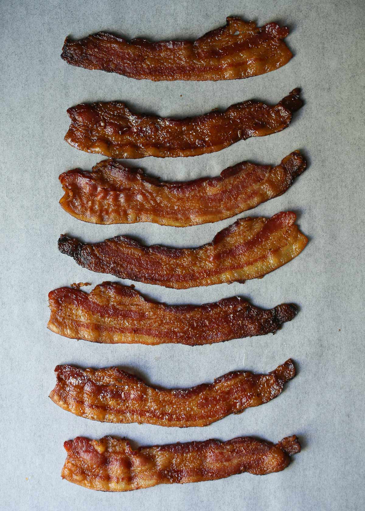 cooked bacon laid out on parchment paper.