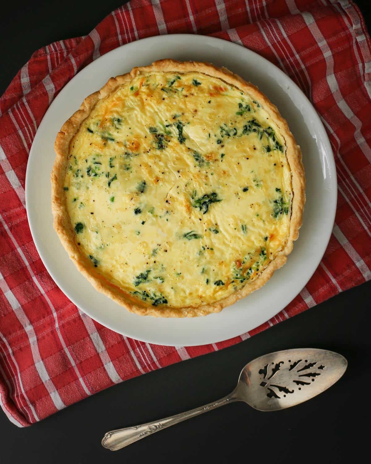 fully baked quiche florentine on red and white cloth with pie server.