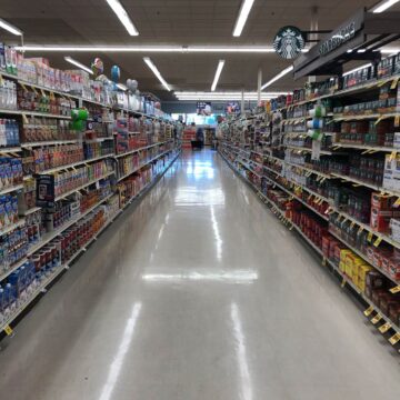 a grocery aisle, empty of people, with a starbucks sign hanging near the coffee display.