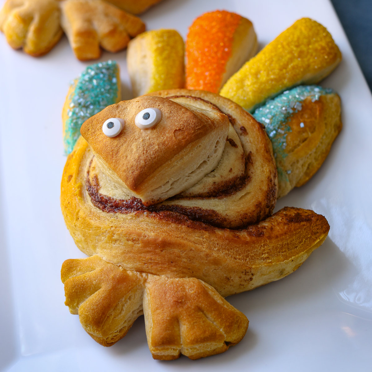 baked cinnamon roll turkey with candy eyes on white tray.