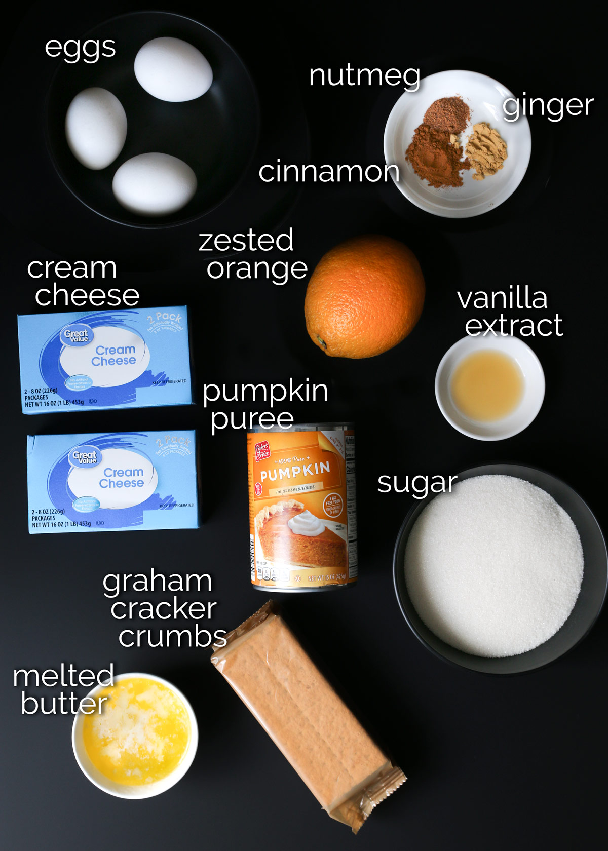 ingredients for pumpkin cheesecake laid out on a black table.