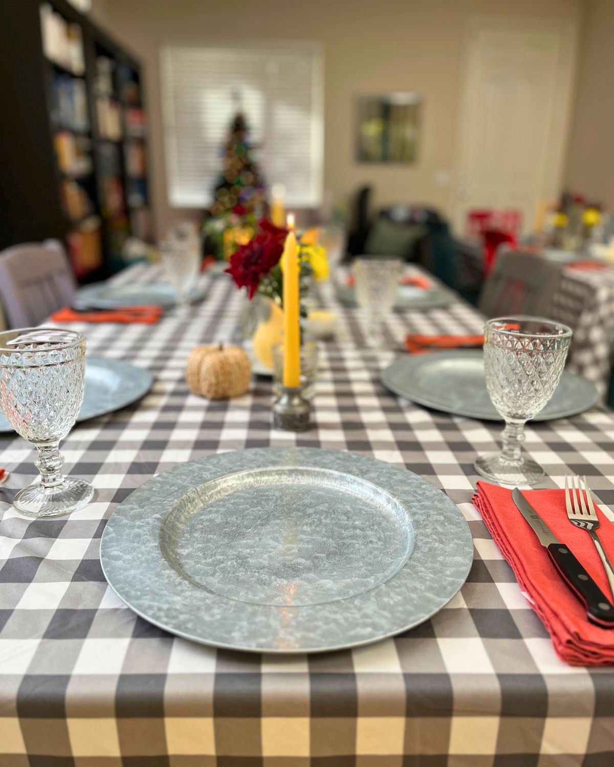 thanksgiving table set with chargers and fall decor, with a Christmas tree in the background.