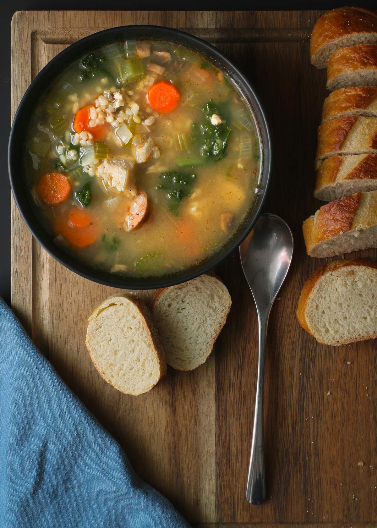 overhead shot of a bowl of soup on a board with a spoon, napkin, and sliced bread.