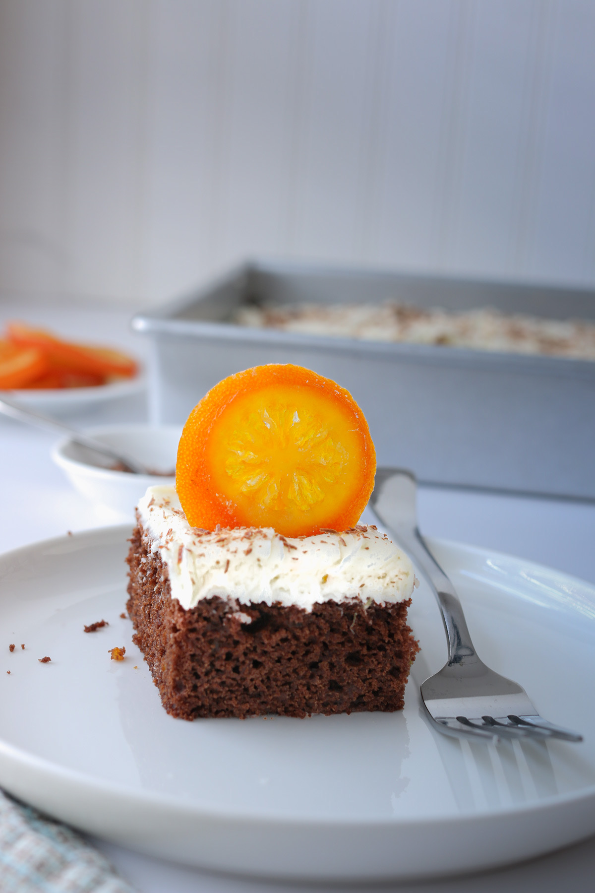 square of chocolate orange cake on white plate with fork on table.