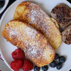 plate of brioche French toast, with sausages and berries.