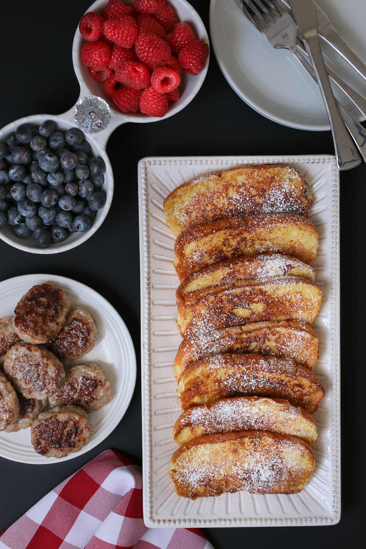 platter of French toast with dishes of berries and sausages.