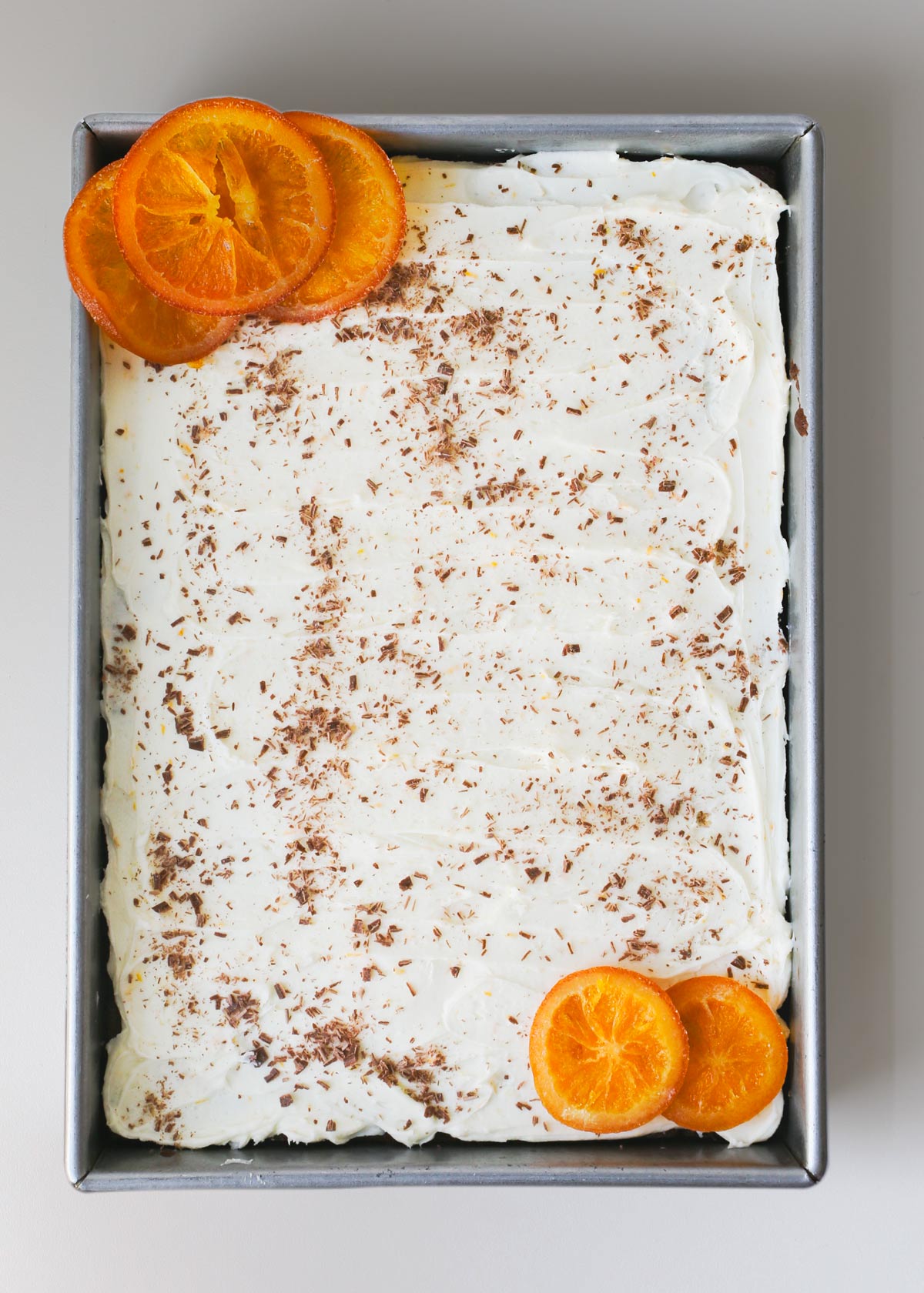 overhead shot of chocolate cake with orange frosting in silver baking pan.