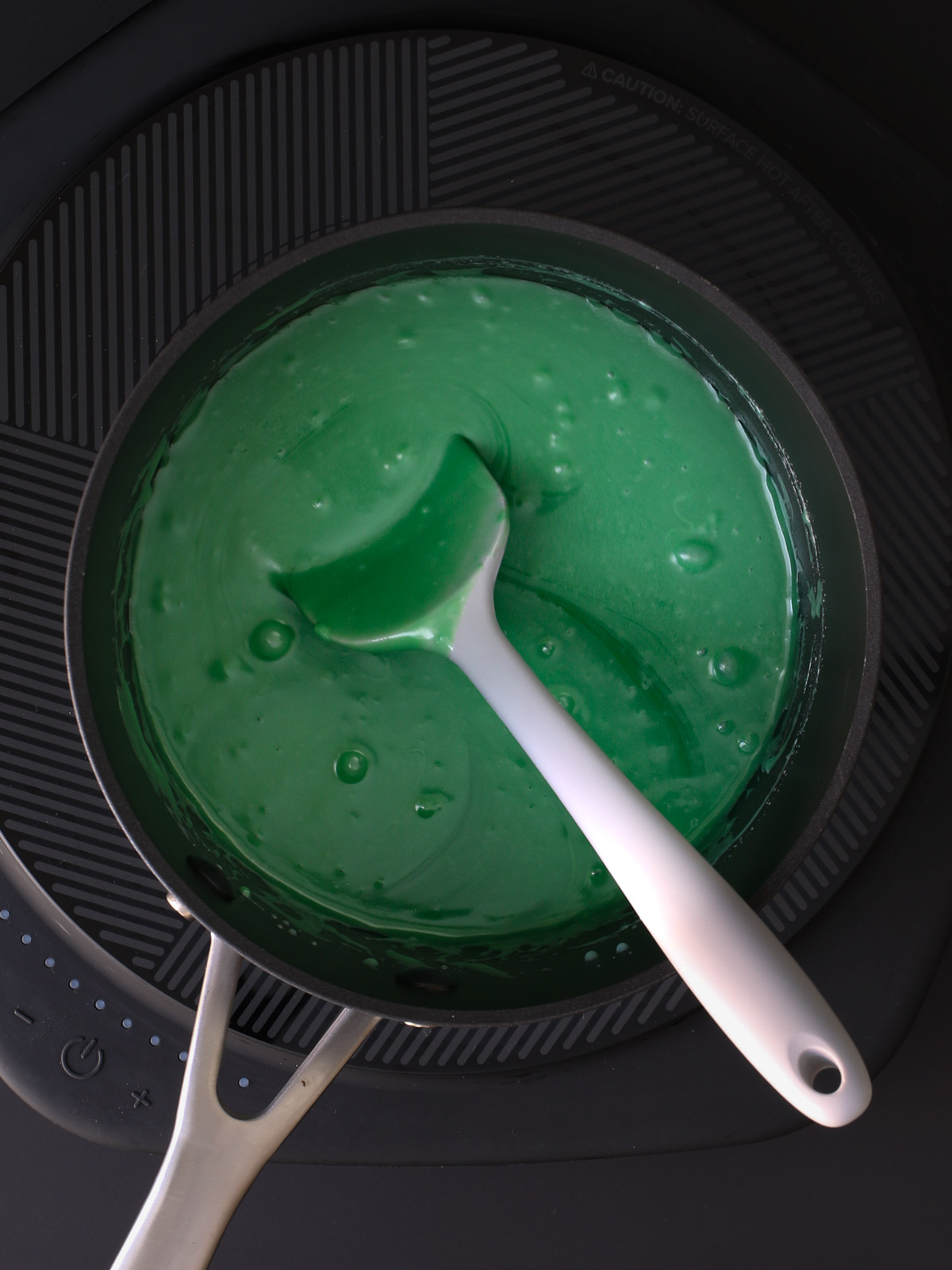 stirring the melted mixture in a saucepan with gray spatula.