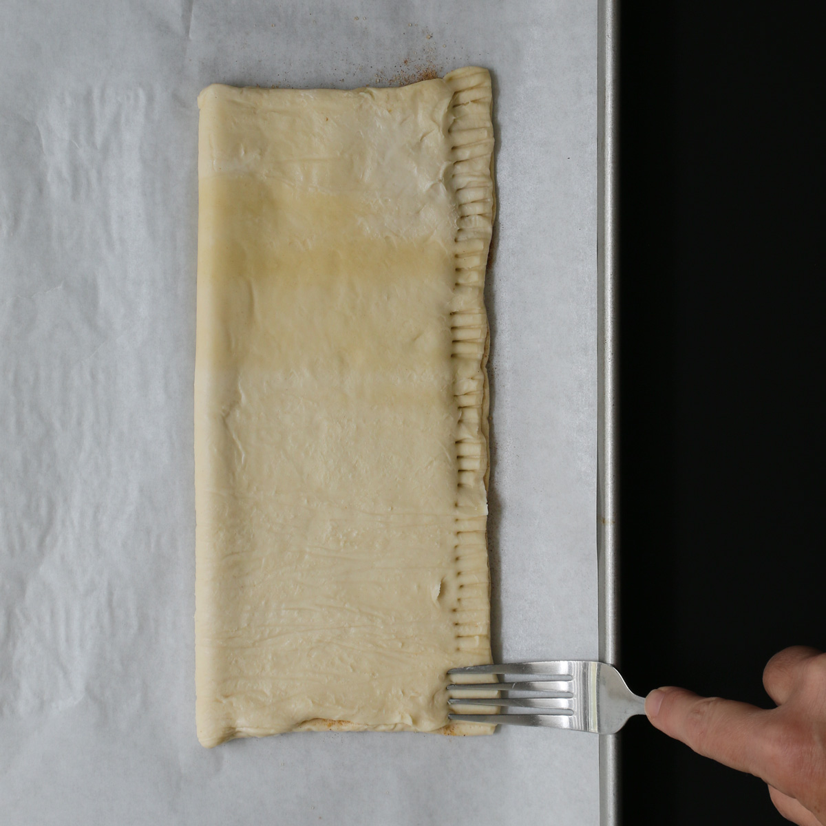puff pastry folded in half and being crimped on long edge with fork.