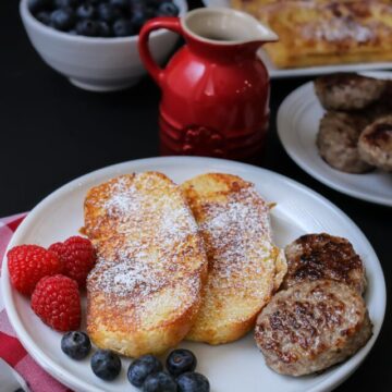 breakfast table set with French toast, sausages, and berries.