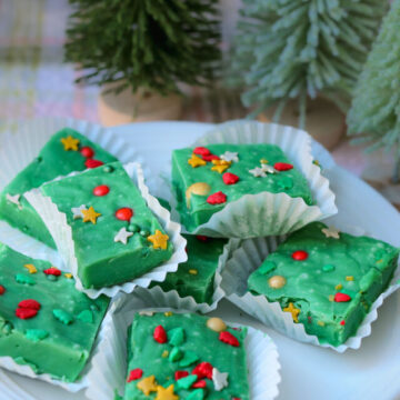 plate of Christmas Fudge squares on white paper cups near small Christmas trees.