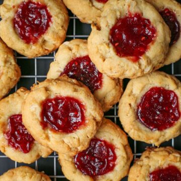 raspberry thumbprint cookies piled on a cooling rack.