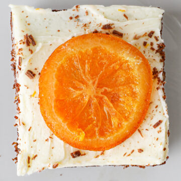 square of cake topped with orange buttercream and a slice of candied orange.
