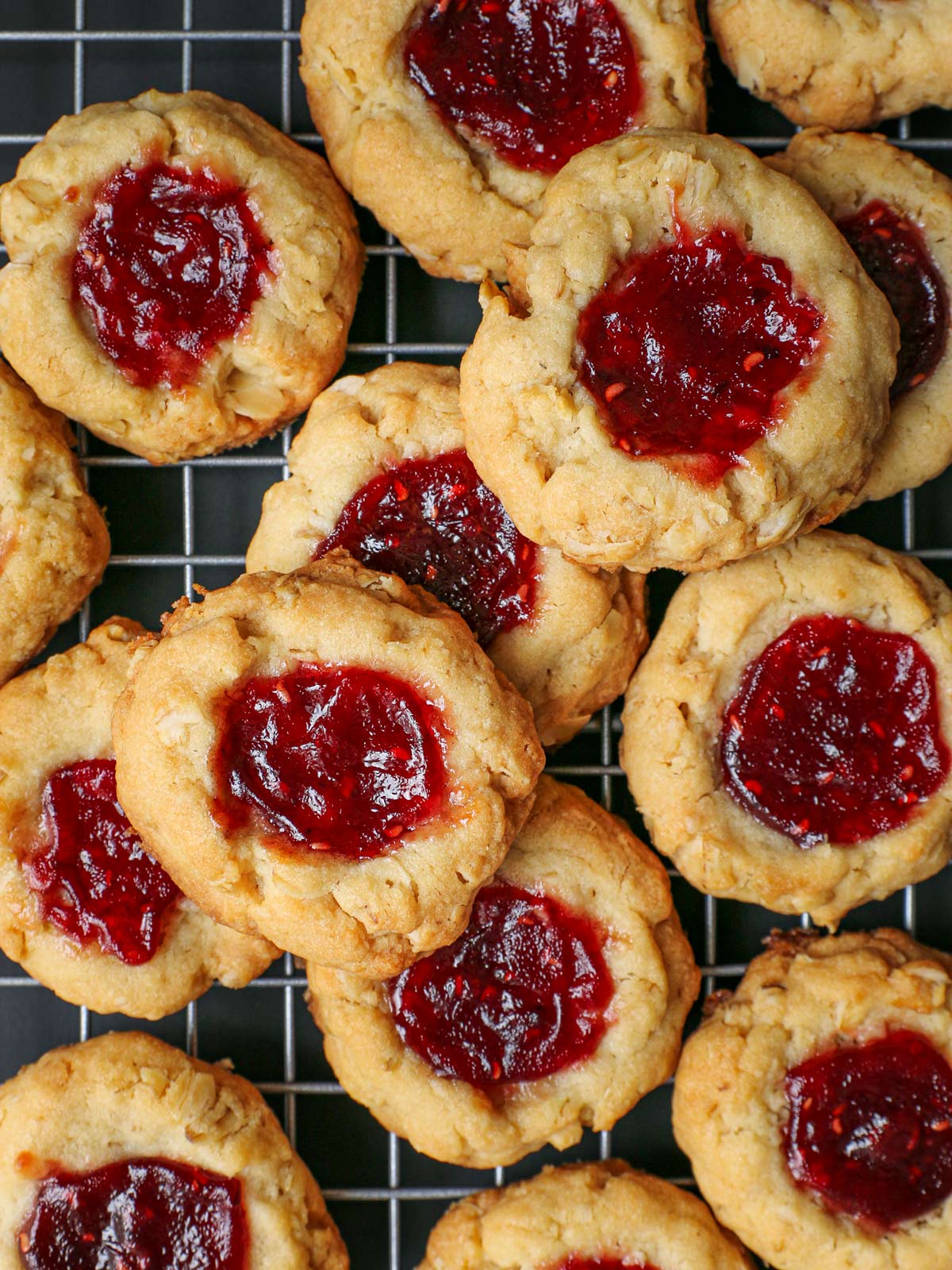 raspberry thumbprint cookies piled on a cooling rack.
