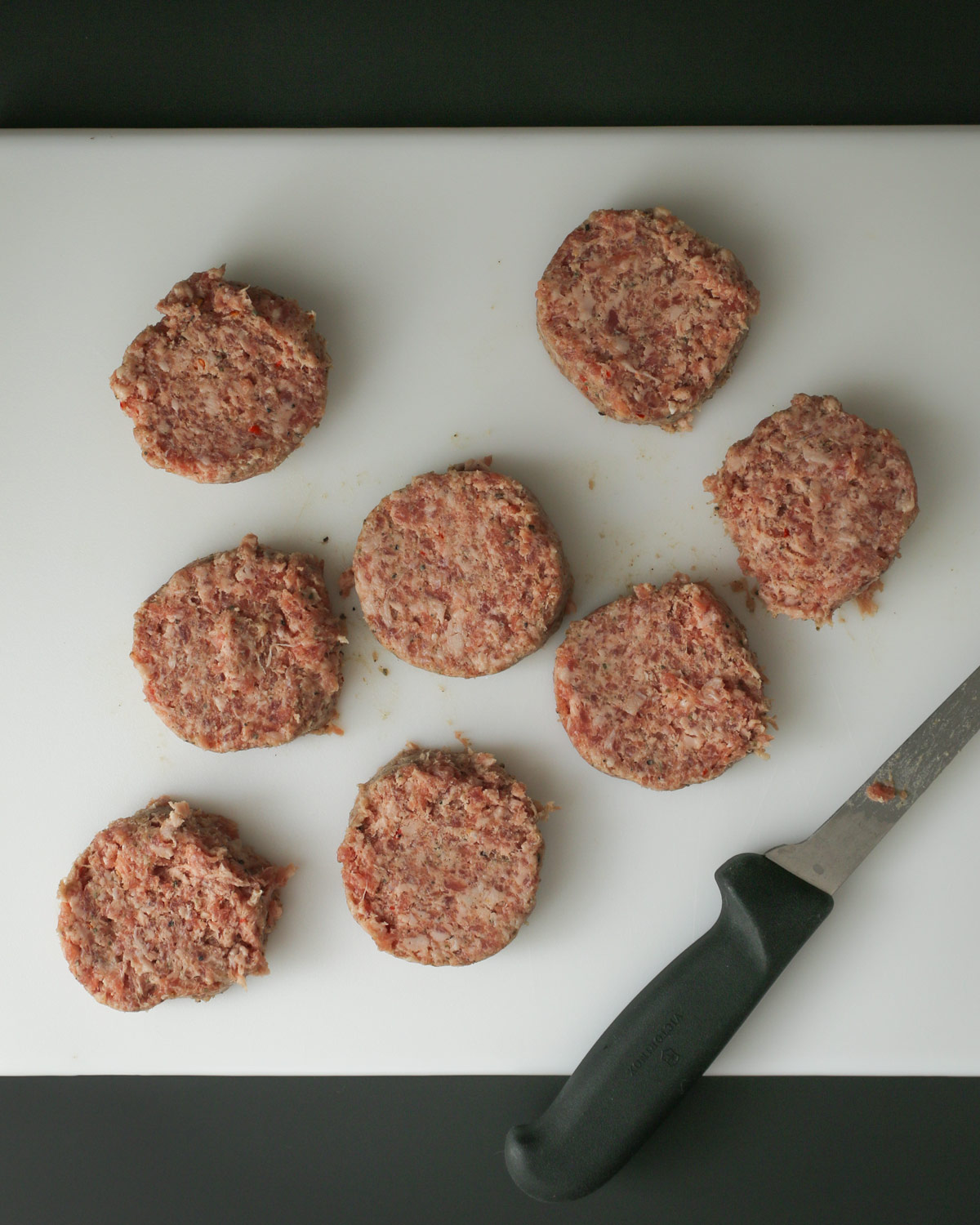 eight sausage patties on cutting board with knife nearby.