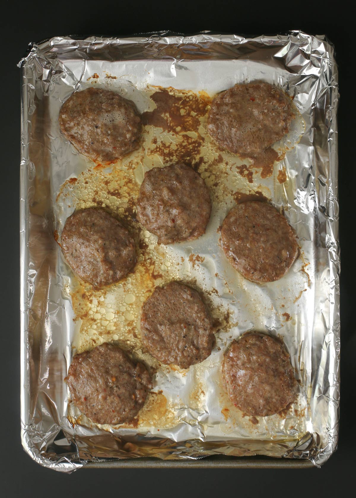 cooked sausage patties on foil in baking sheet.