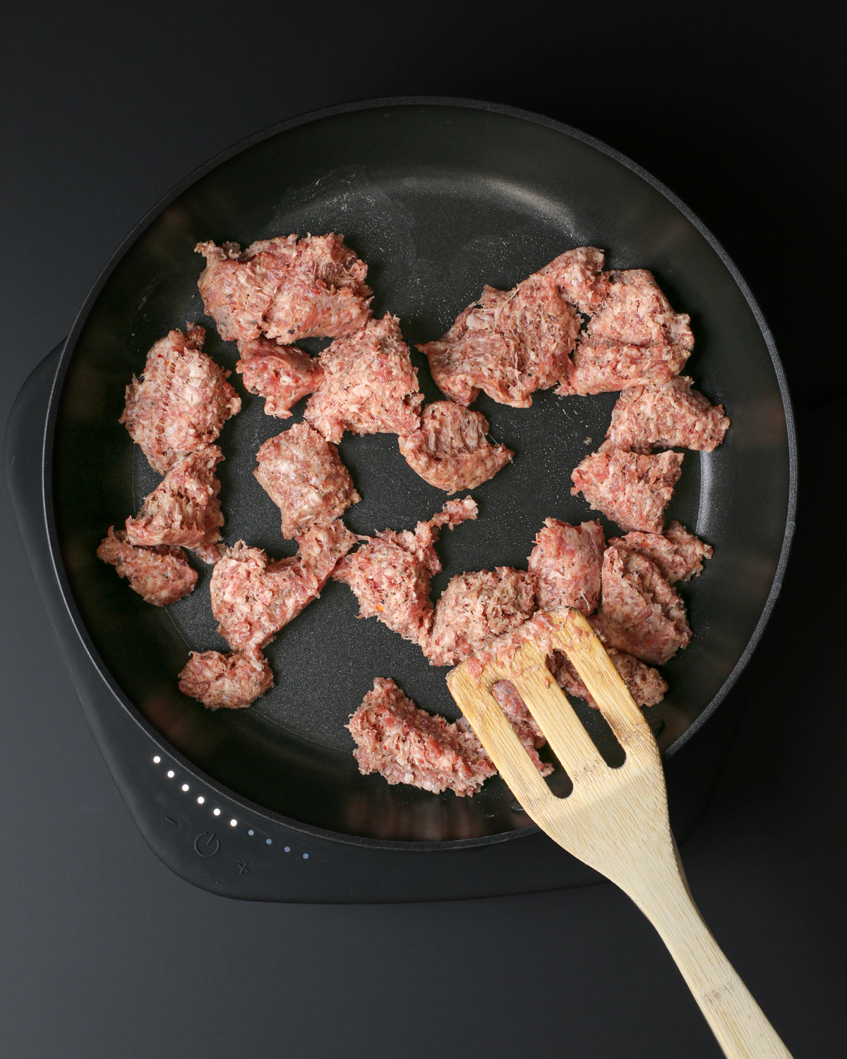 sausage crumbles in skillet with wooden spatula.