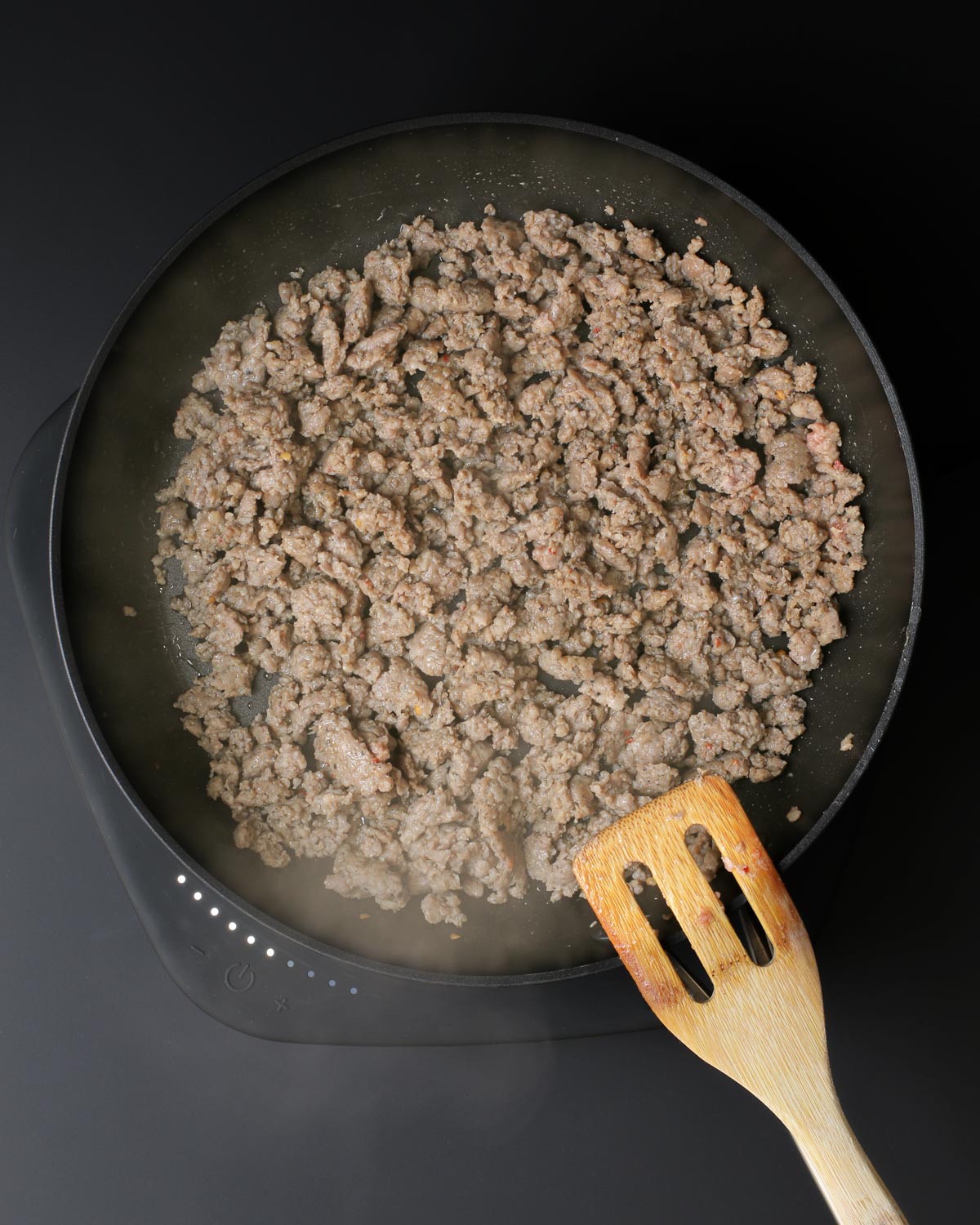 cooked sausage crumbles in skillet with wooden spatula.