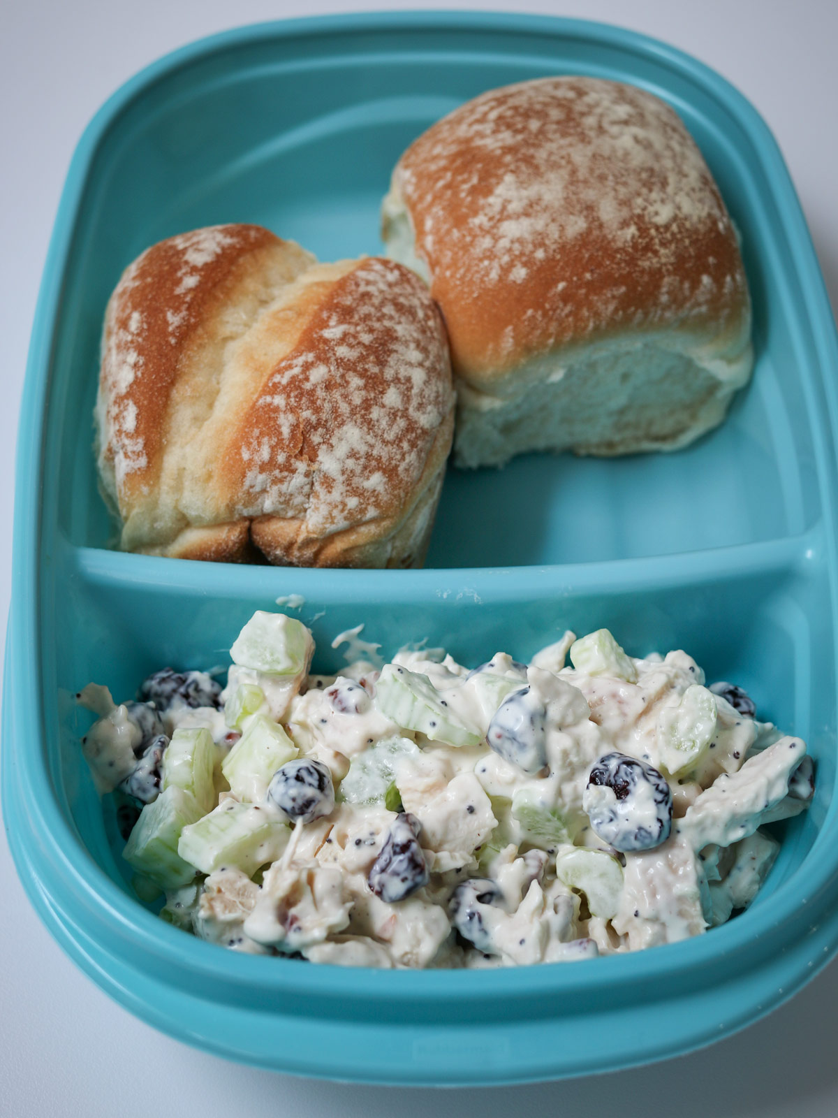 chicken salad in meal prep box with two rolls.