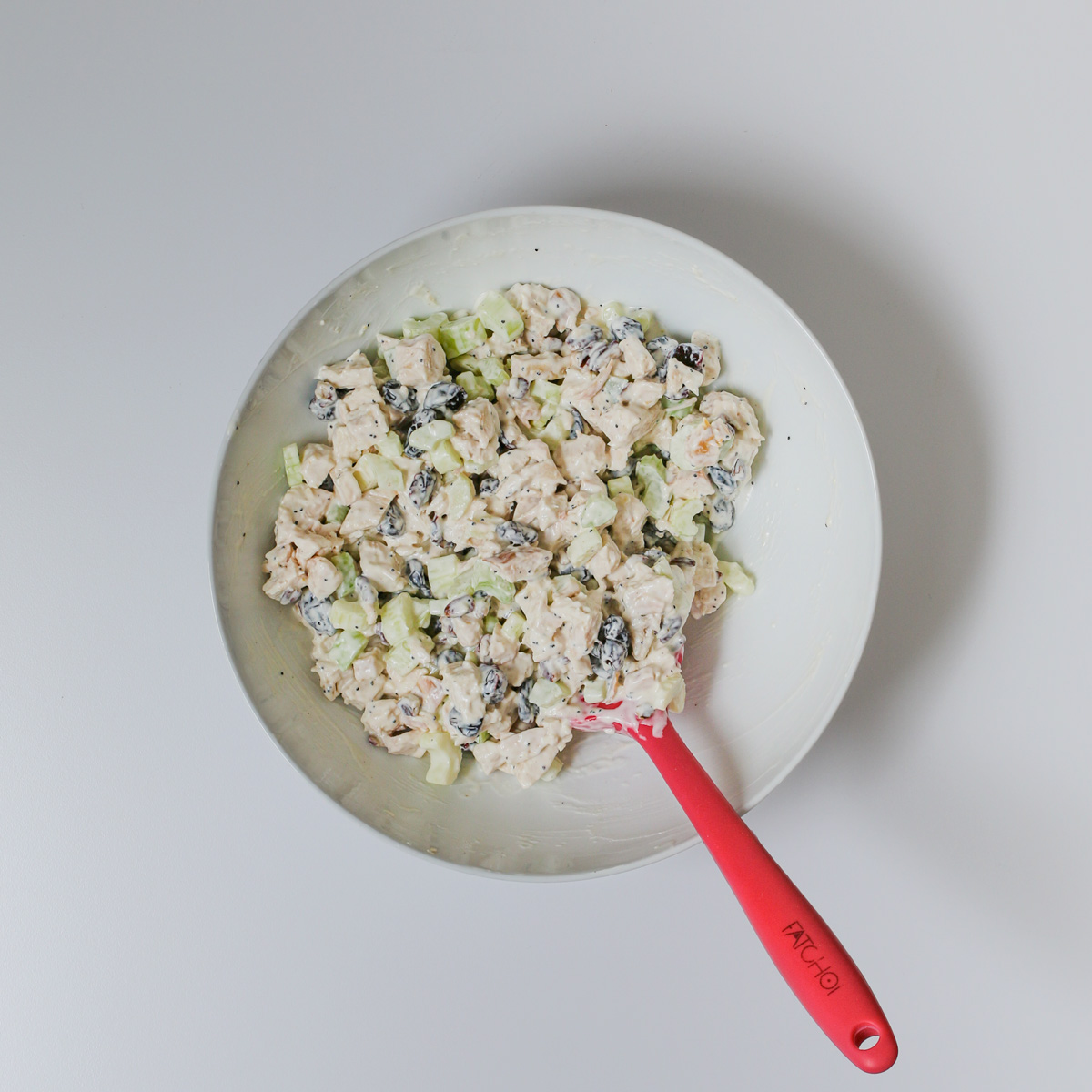 chicken salad completed in white bowl with red spatula.