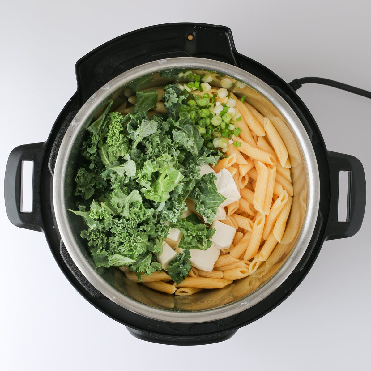adding cream cheese cubes and chopped kale to cooked pasta in instant pot.