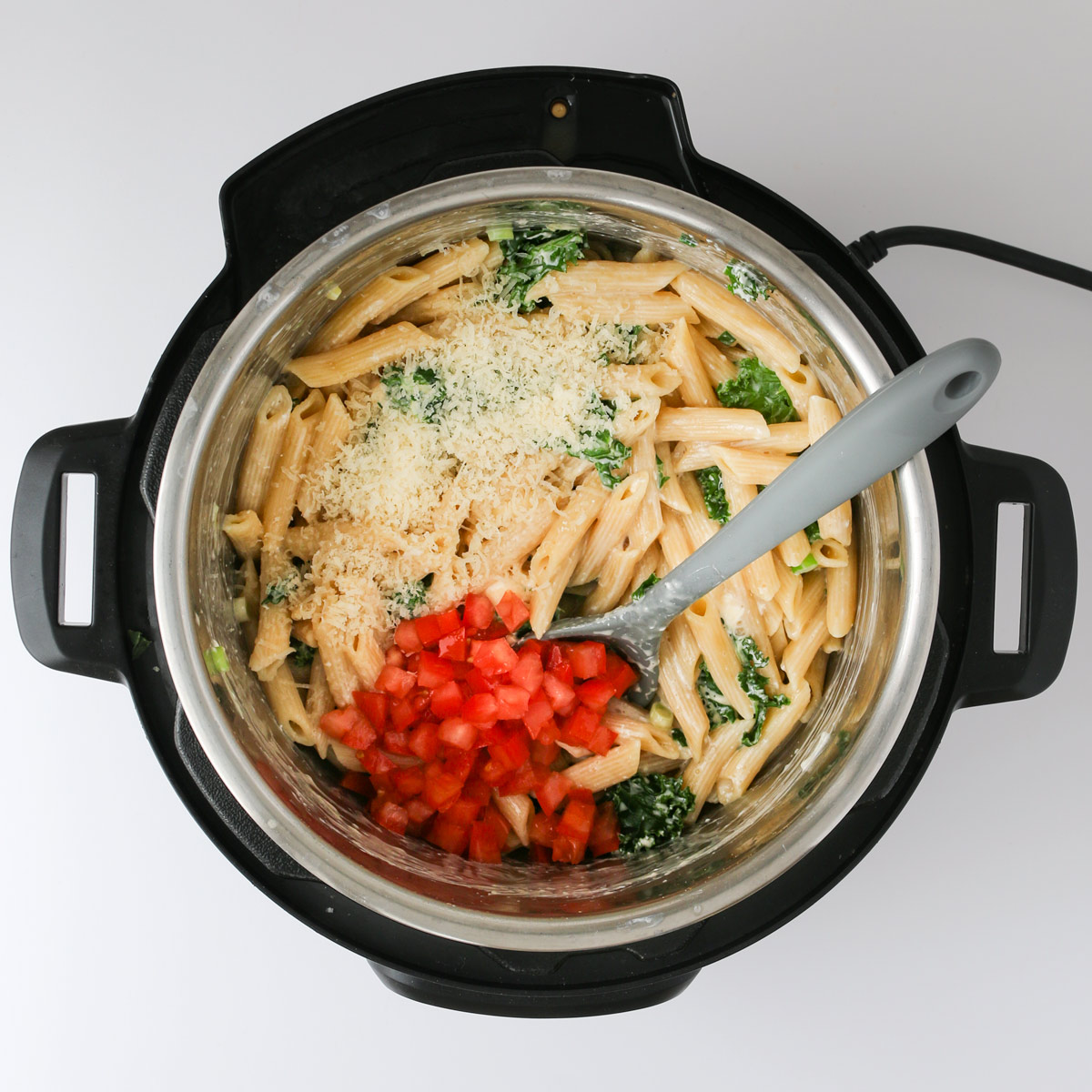 adding tomatoes and parmesan to pasta mixture in instant pot.