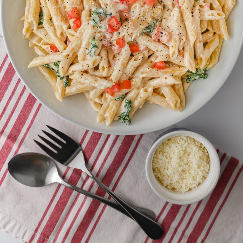 cream cheese pasta in serving bowl next to parmesan and fork and spoon.
