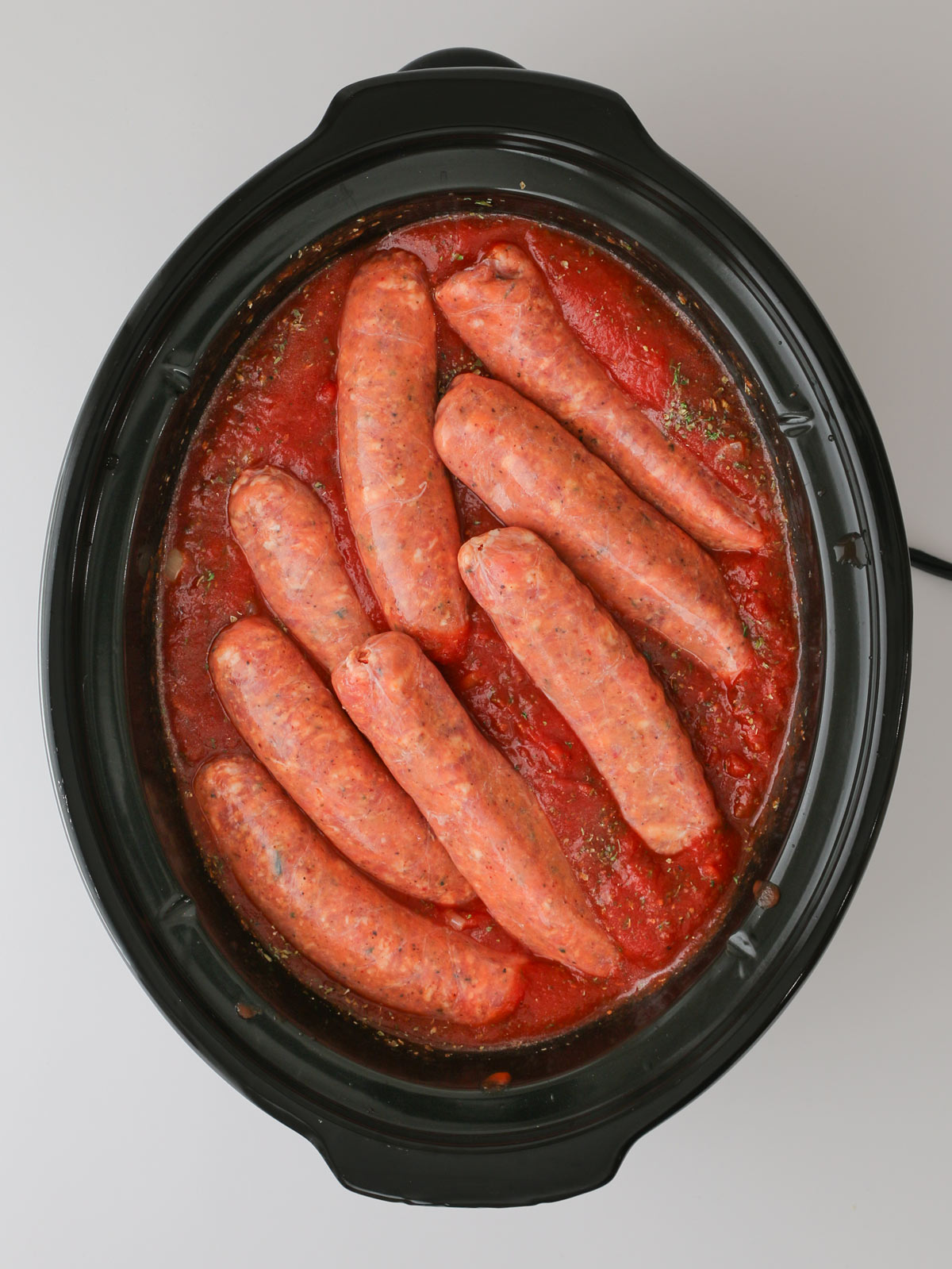 adding the sausage links to the sauce in the crockpot.