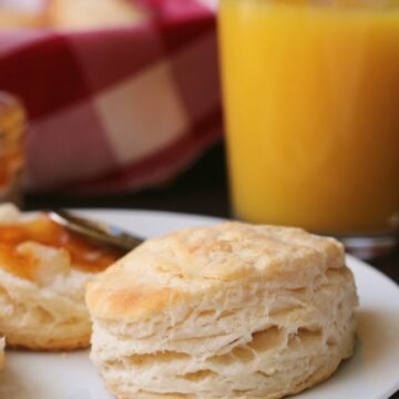 biscuit on a plate with orange juice cup behind.