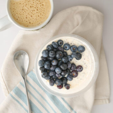 cup of protein overnight oats on cloth with spoon and coffee.