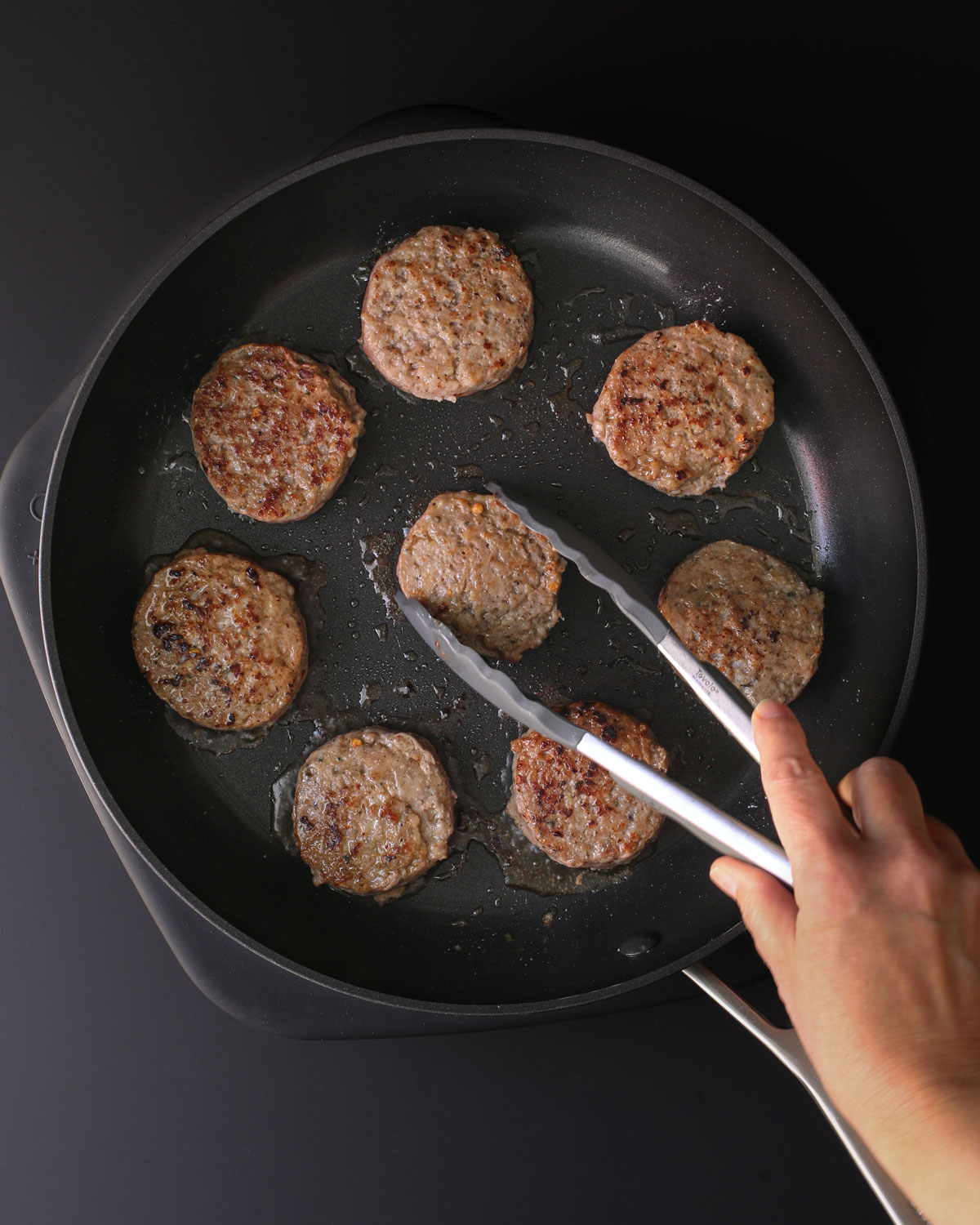 turning browned patties in a skillet with cooking tongs.