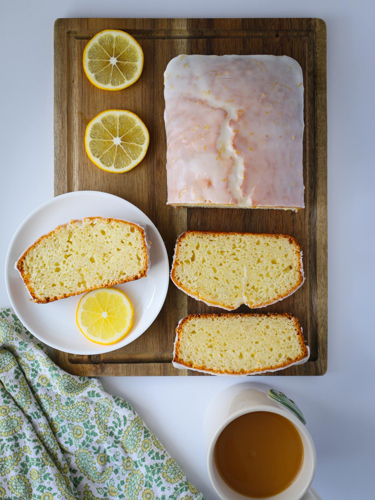glazed lemon loaf on wooden board with slices, and lemon slices, and cup of tea.