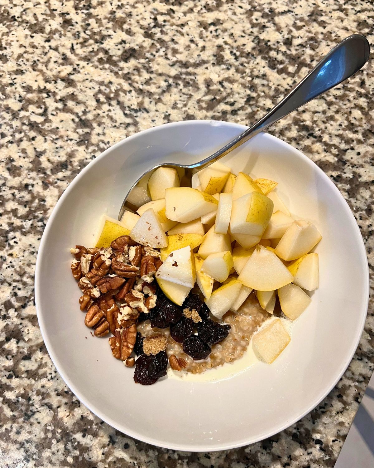 bowl of oats topped with nuts, pears, and dried cherries.