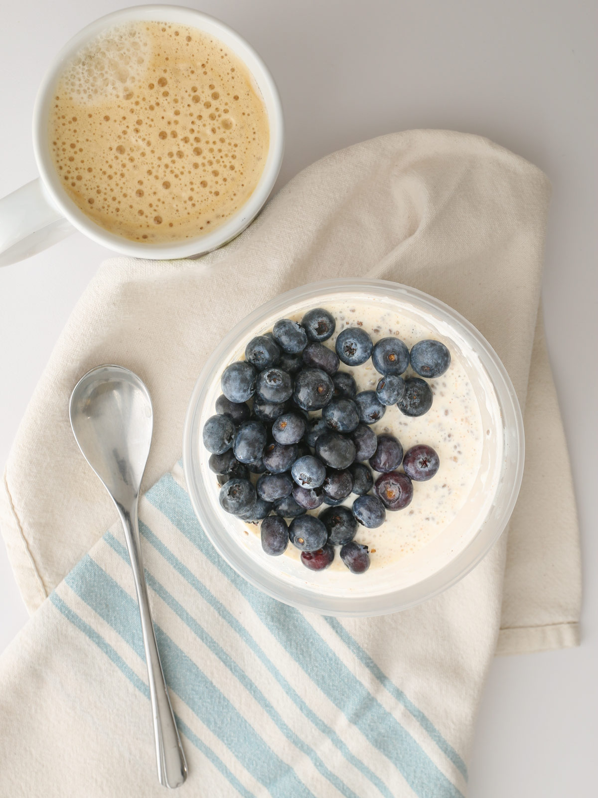 cup of protein overnight oats on cloth with spoon and coffee.